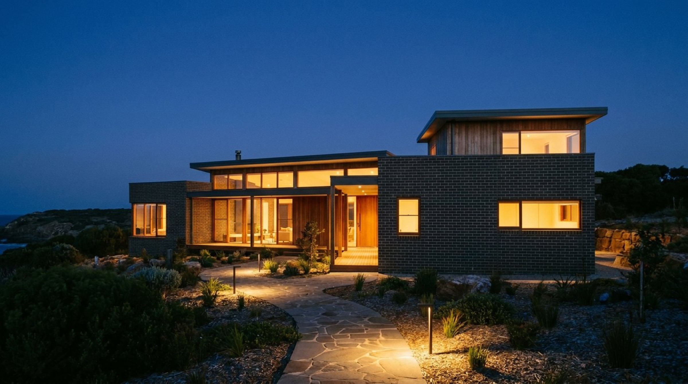 A dark modern home at dusk with warm light through the windows