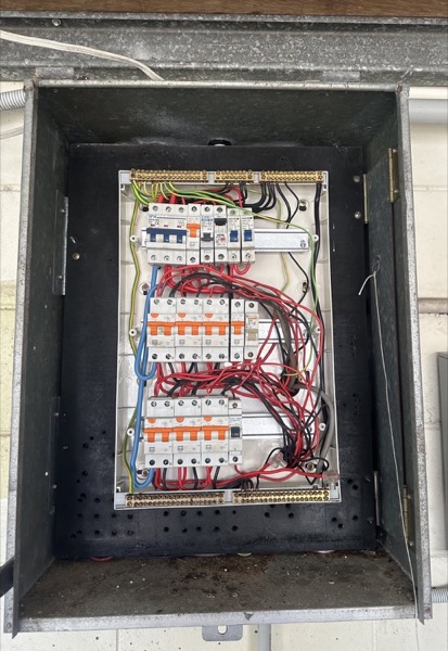 An older switchboard with red and black wiring behind an open steel door