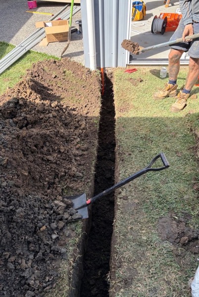A trench cut across a lawn with a spade standing in the soil
