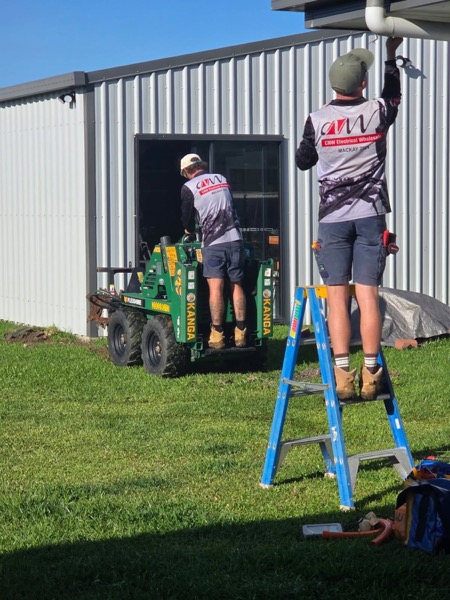 Two workers on ladders at the side of a steel shed