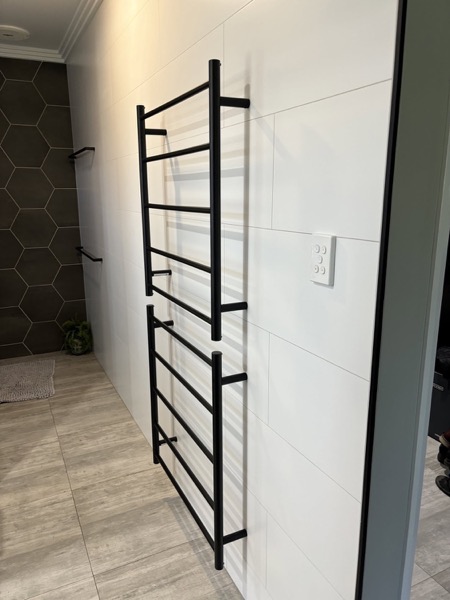 A heated towel rail fitted beside a shower screen